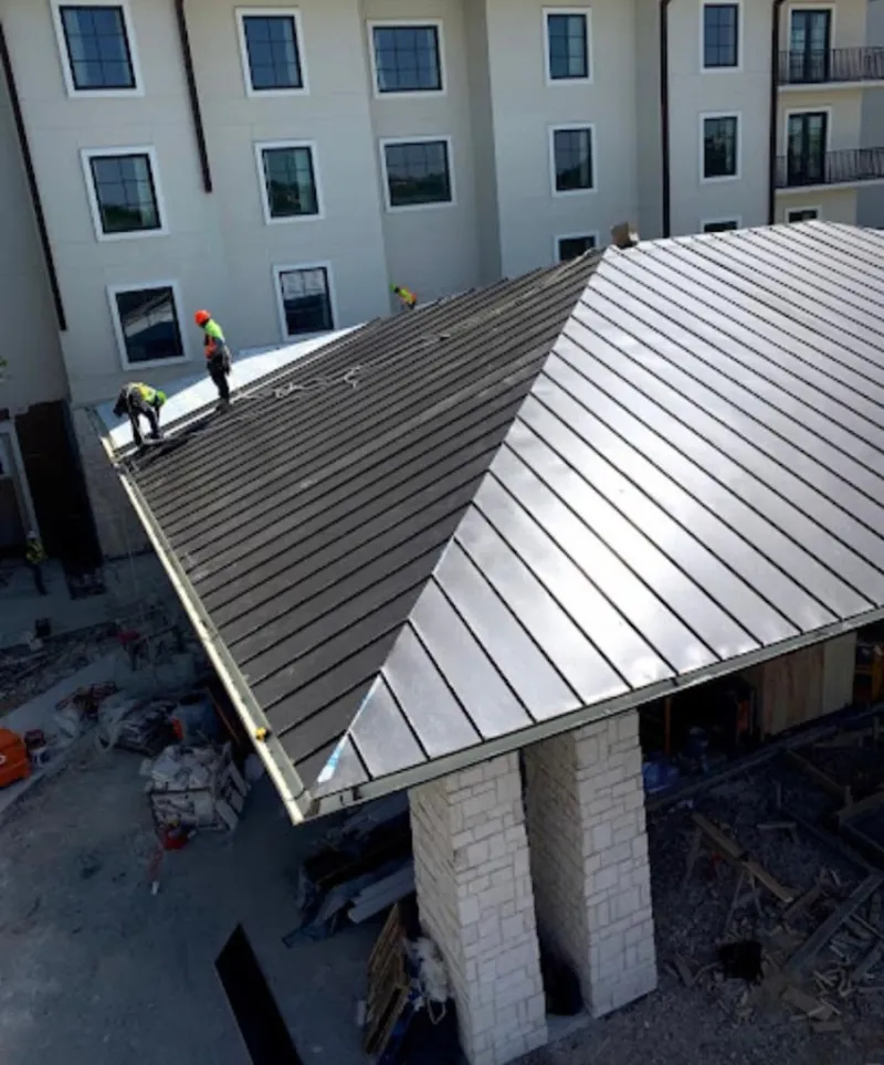Crew installing standing seam metal roof panels on a commercial project in Paola